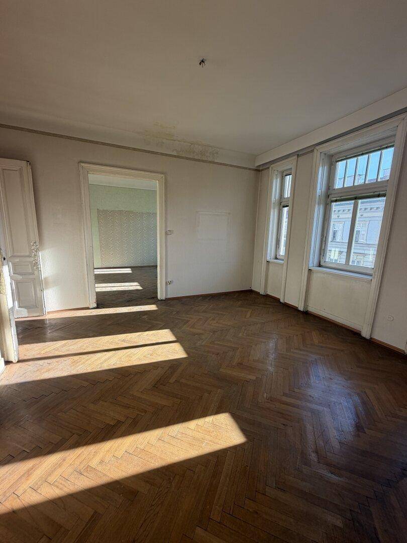 Lichtdurchflutetes Zimmer mit Fischgrätparkett und hohen Fenstern, die den Raum erhellen.