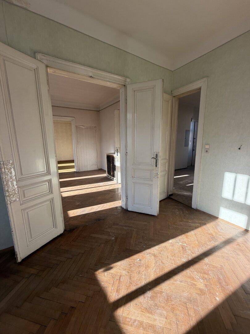 Helles Zimmer mit Fischgrätparkett und doppelten Flügeltüren, die den Blick in weitere Räume freigeben.