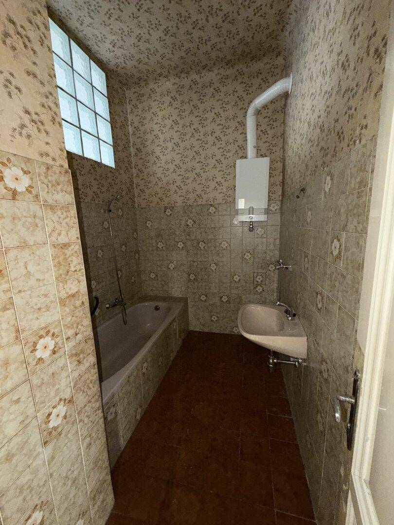 Veraltetes Badezimmer mit Badewanne, Waschbecken und einem Fenster aus Glasbausteinen.