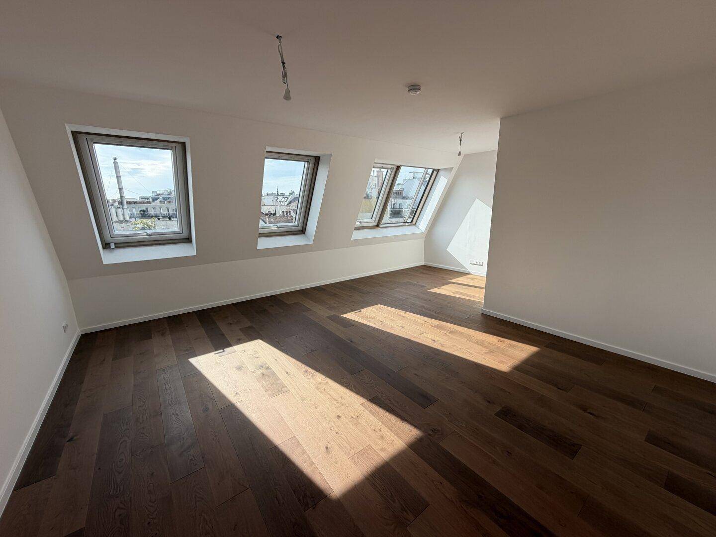 Helles, unmöbliertes Zimmer im Dachgeschoss mit Holzboden und mehreren Dachfenstern.