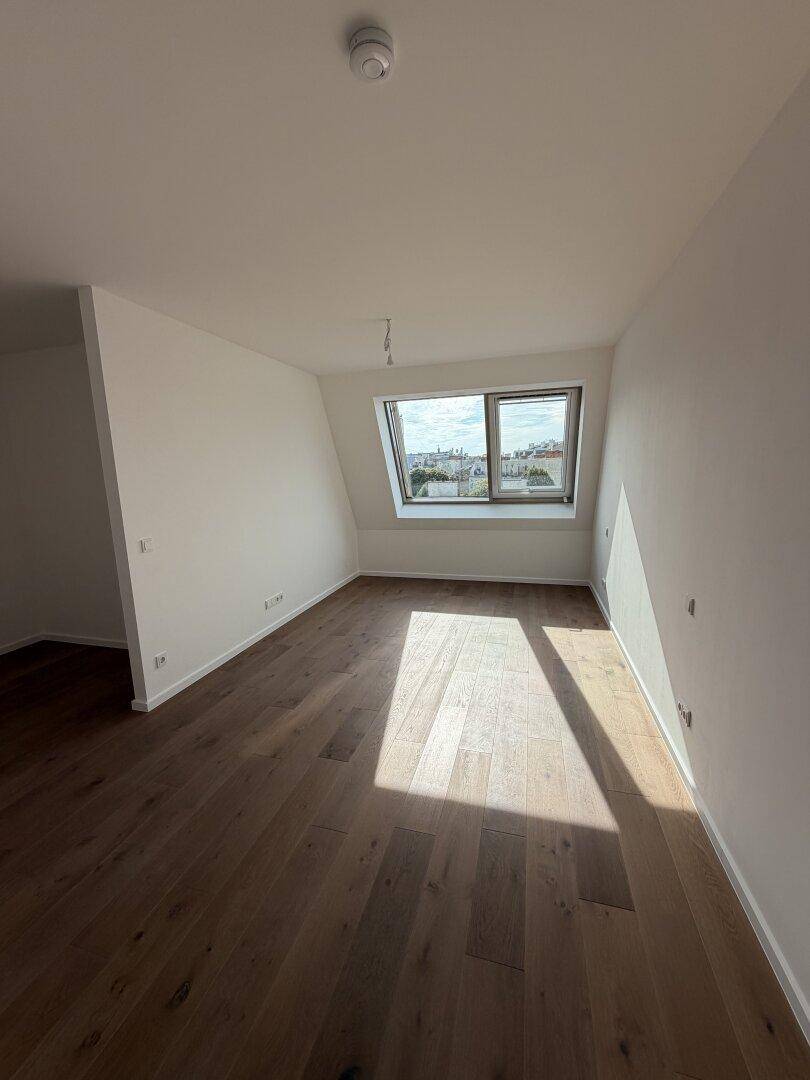 Helles, unmöbliertes Zimmer im Dachgeschoss mit Holzboden und einem großen Dachfenster.