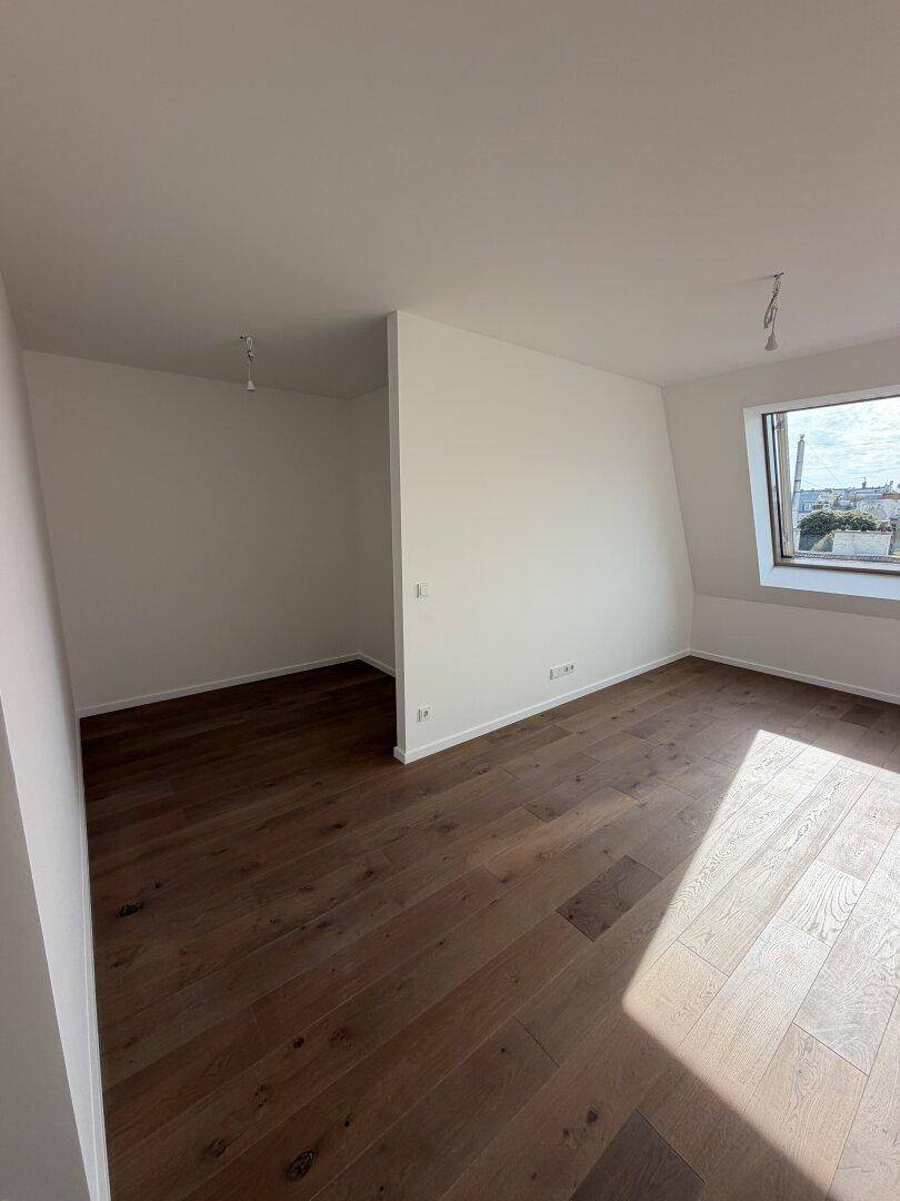 Geräumiges, unmöbliertes Zimmer mit Holzboden, Dachfenster und offenem Zugang zu einem Nebenraum.
