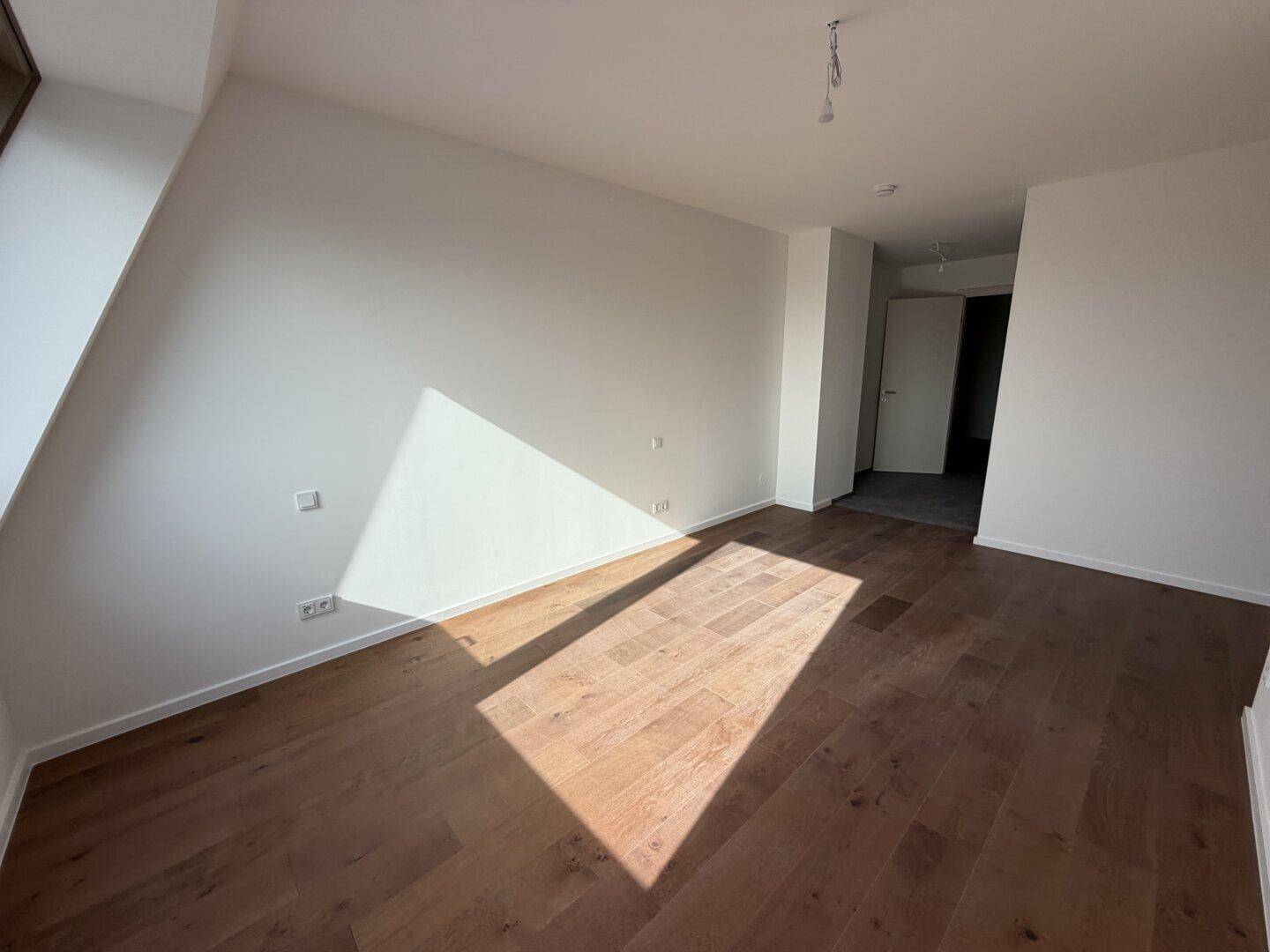 Unmöbliertes Zimmer mit Holzboden, Dachschräge und hellem Lichteinfall.