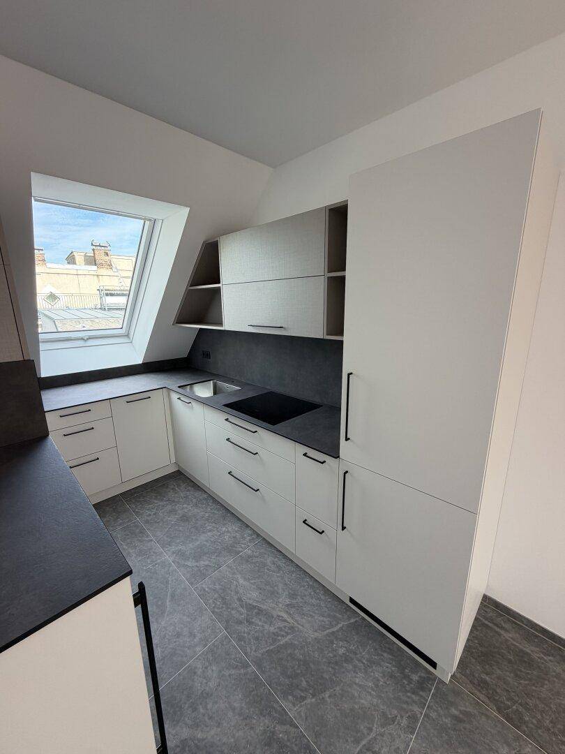Moderne Einbauküche mit weißen Schränken, dunkler Arbeitsplatte und Dachfenster.