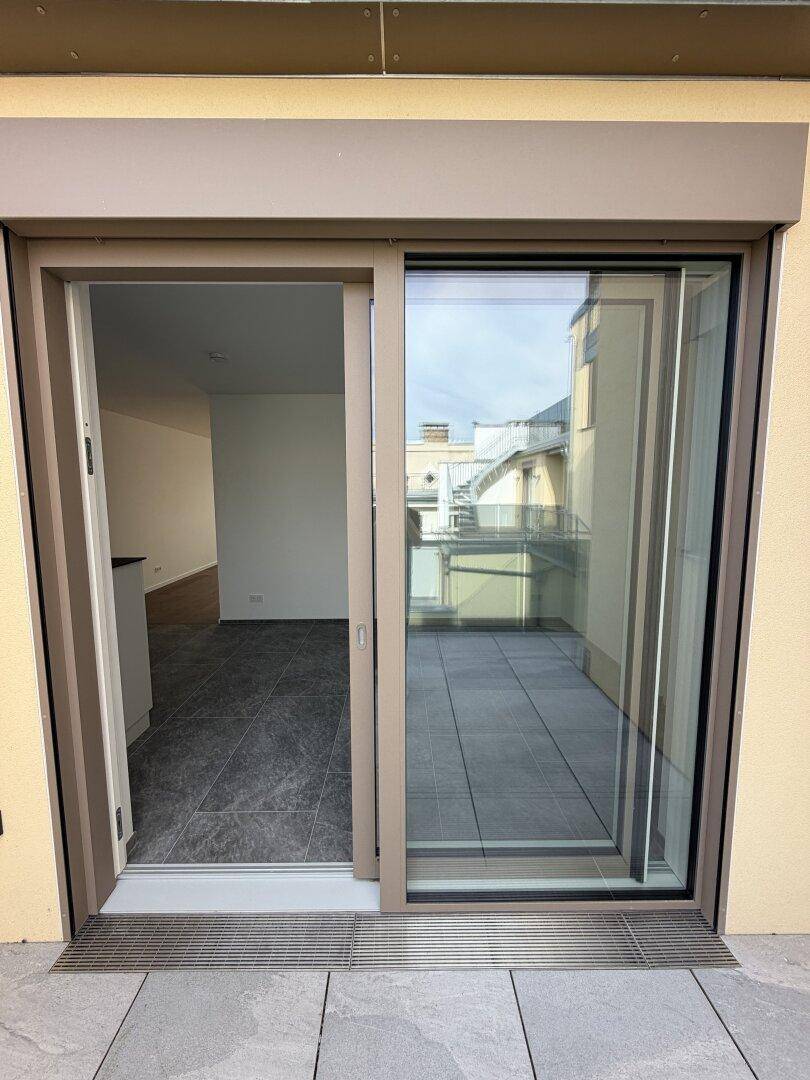 Zugang zu einer gefliesten Terrasse mit Schiebetür und Außenjalousien.