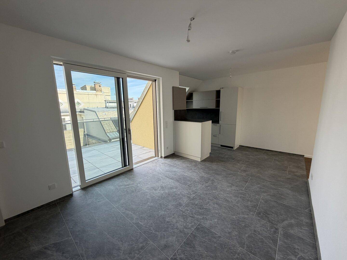 Heller Wohnbereich mit Zugang zur Terrasse und offener Küche im Hintergrund.