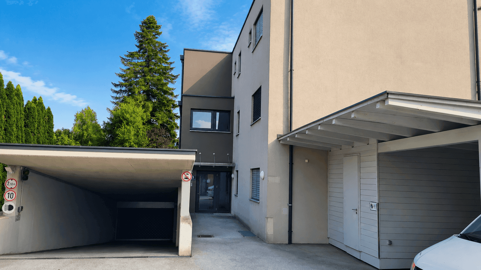 Moderne Wohnanlage mit Tiefgaragenzufahrt und überdachtem Carport-Parkplatz.