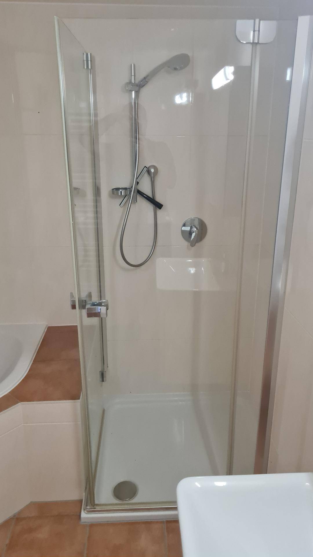 Duschkabine mit Glaswand und moderner Duscharmatur in einem gefliesten Badezimmer.