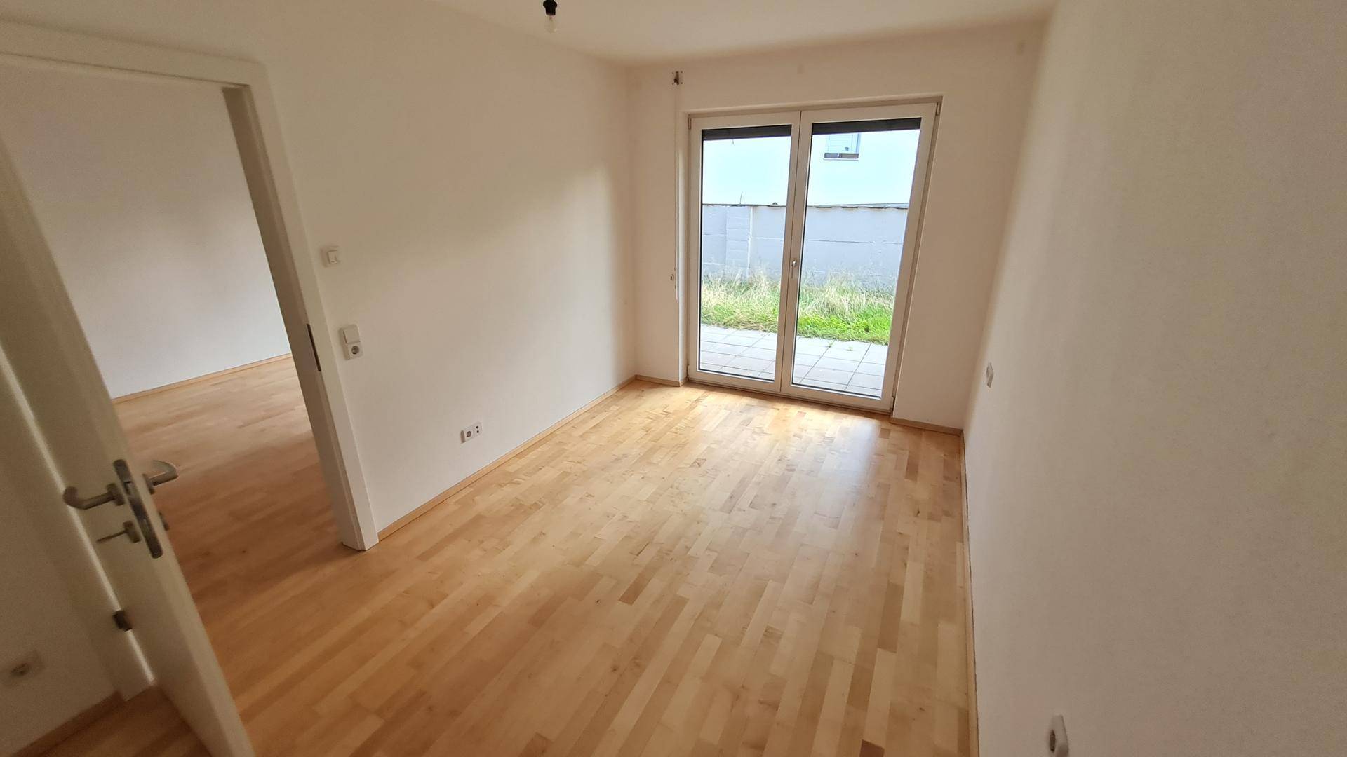 Heller Raum mit Holzboden und Zugang zu einem Außenbereich durch eine große Glastür.