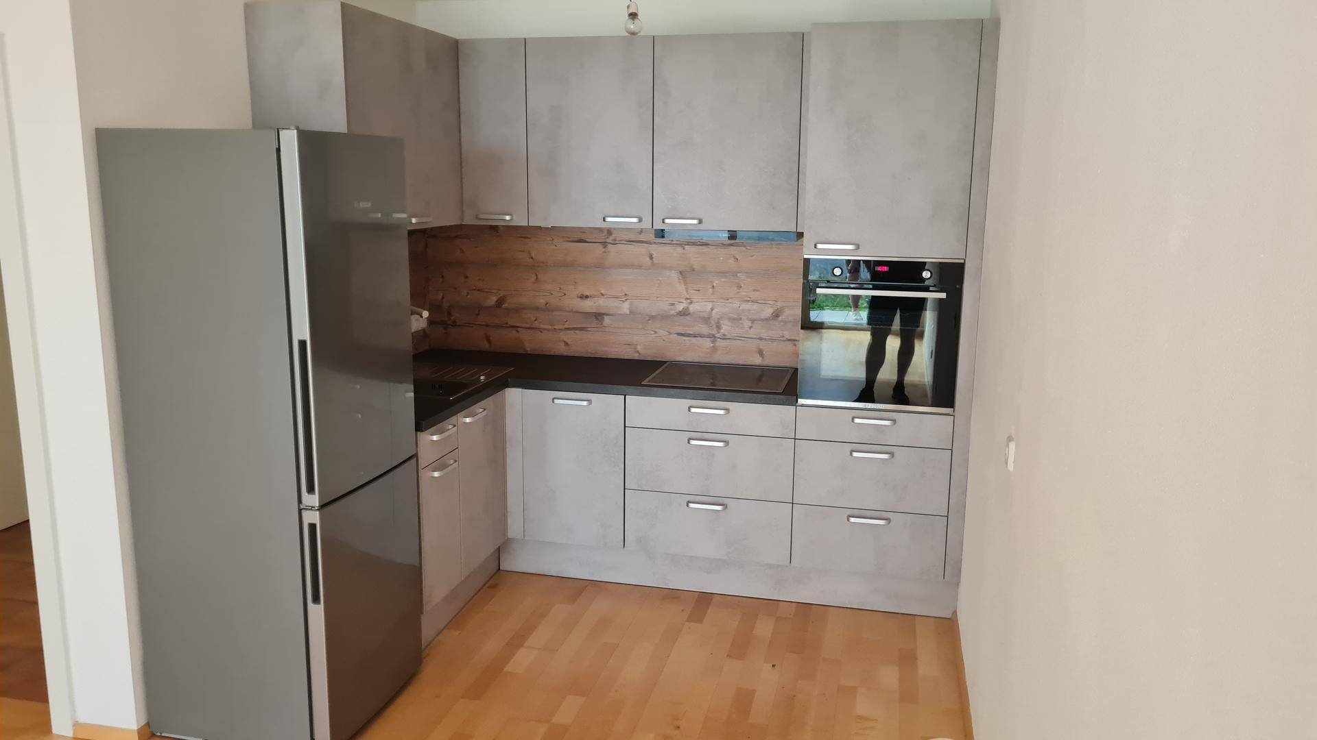 Moderne Einbauküche mit grauen Schränken, Holzrückwand, Induktionskochfeld und integriertem Backofen.