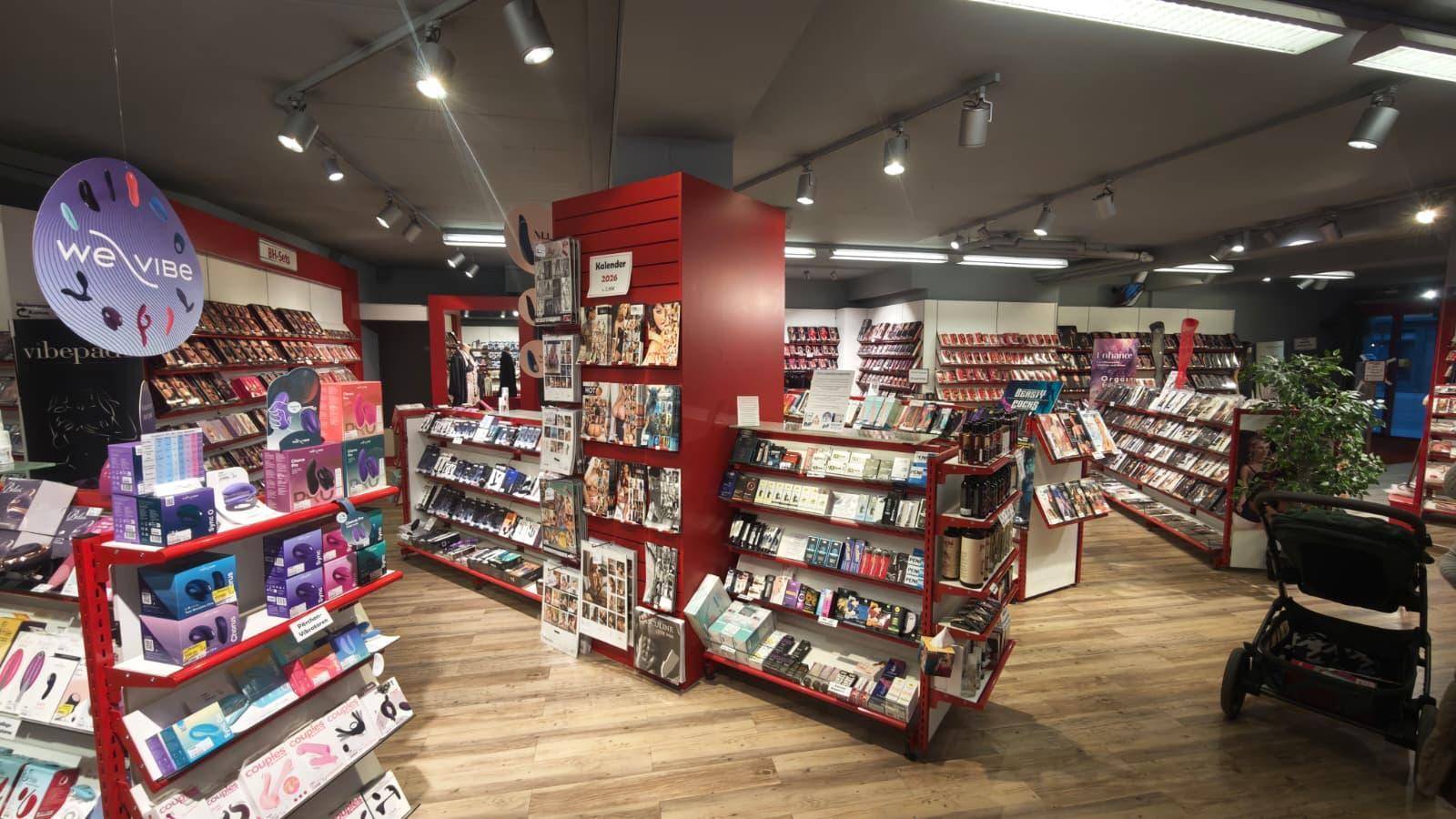 Heller Verkaufsraum mit vielfältigen Produktpräsentationen in roten und weißen Regalen auf einem Holzfußboden.