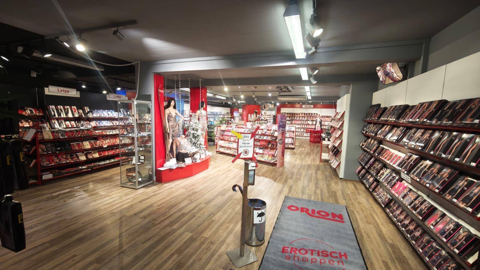 Geräumiger Verkaufsraum mit Holzfußboden, Regalen voller Produkte und roter Akzentbeleuchtung in einem modernen Ambiente.