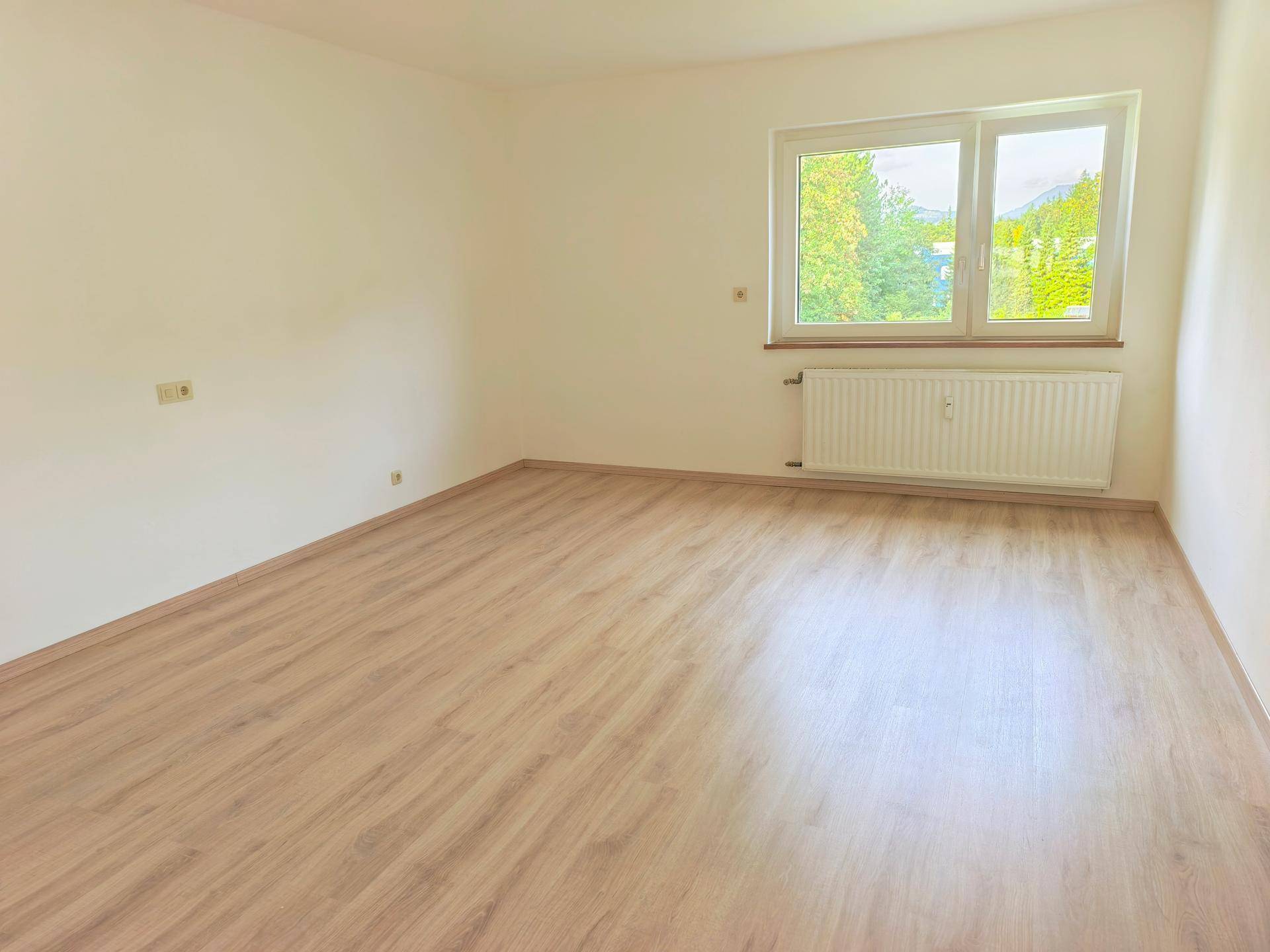 Geräumiger, heller Raum mit Laminatboden und großem Fenster mit Ausblick.
