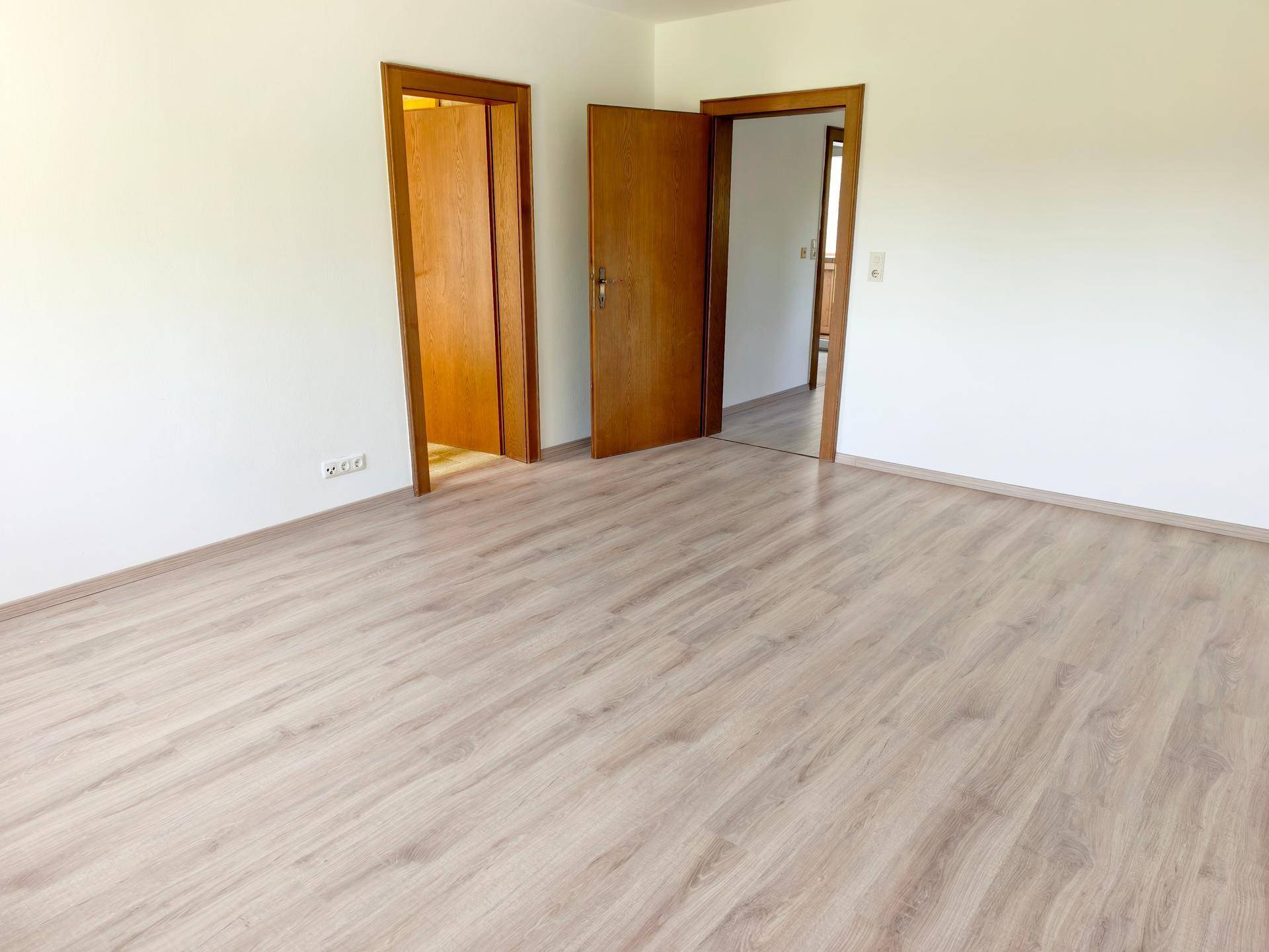 Heller Raum mit Laminatboden und mehreren Holztüren, der verschiedene Bereiche verbindet.