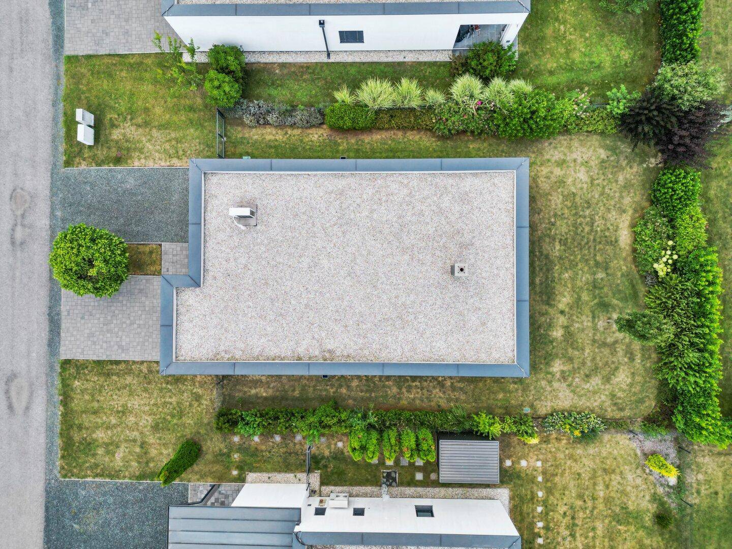Draufsicht auf ein modernes Flachdachhaus mit Kiesdach und angelegtem Gartenbereich.
