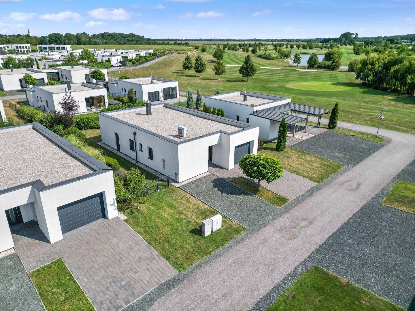 Reihe moderner Häuser mit Flachdächern, Garagen und Blick auf den Golfplatz.