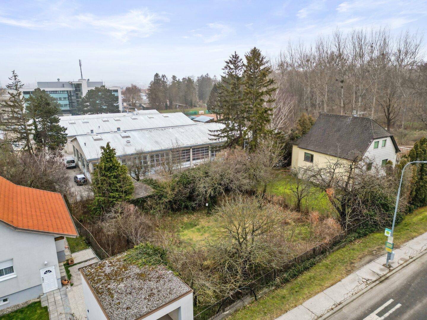 Übersicht des Grundstücks mit angrenzenden Gebäuden, viel Grün und einem Wald im Hintergrund.