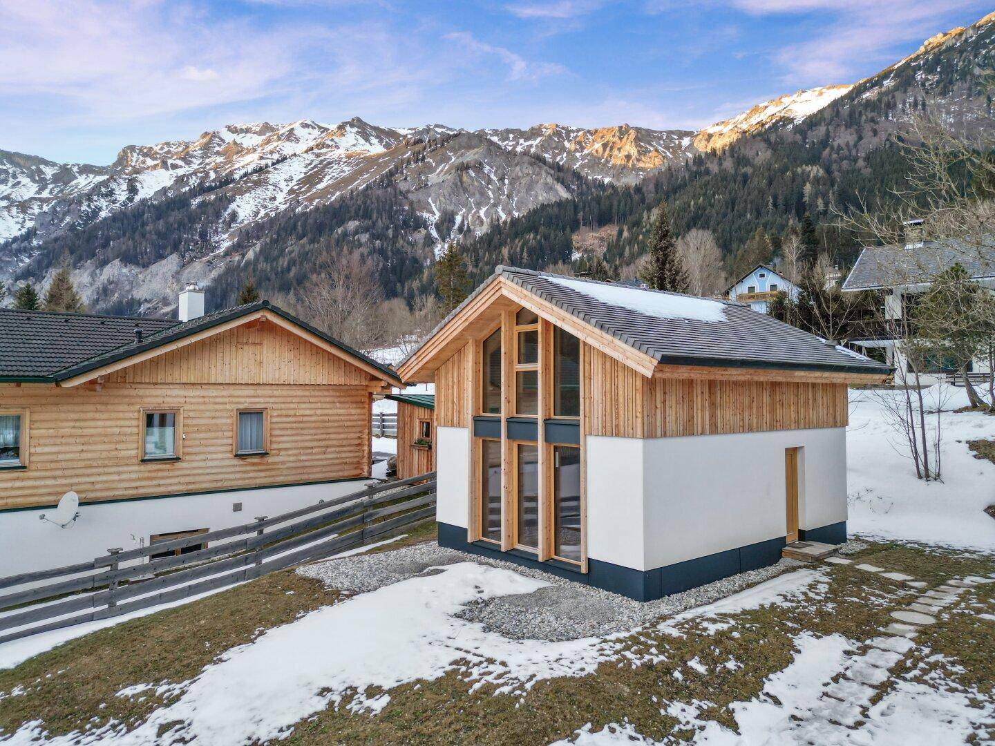 Einzelnes modernes Chalet mit großen Fenstern und Holzfassade, eingebettet in eine verschneite Berglandschaft.