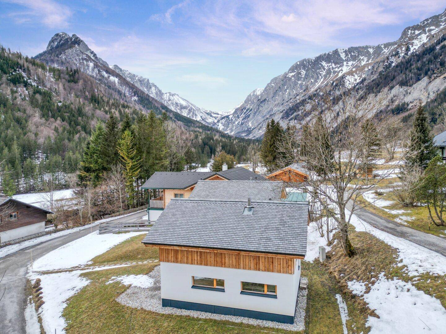 Luftaufnahme eines Chalets mit Satteldach und Blick auf die umliegende verschneite Bergwelt.