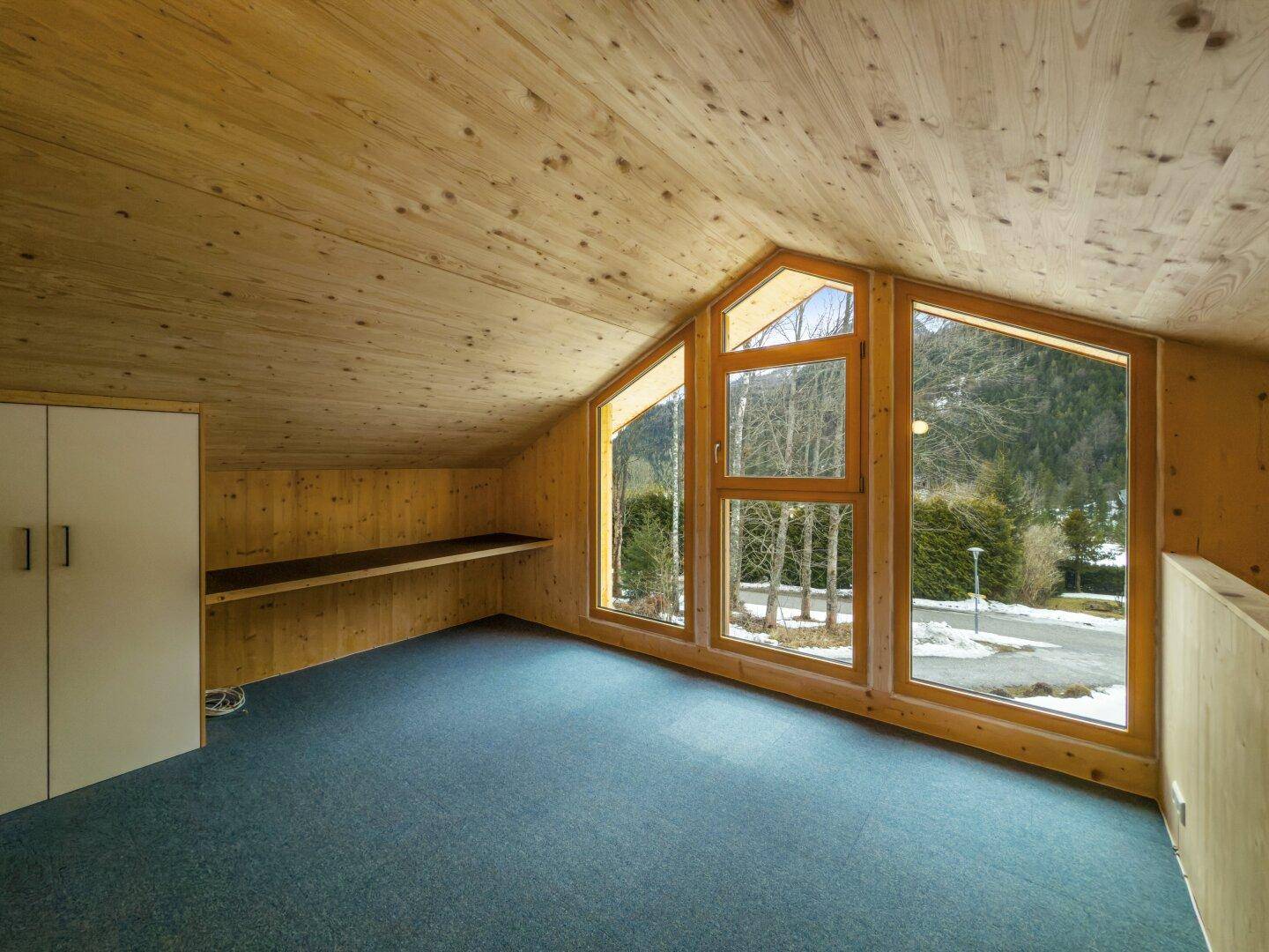 Gemütliches Schlafzimmer im Obergeschoss mit Holzverkleidung, schrägen Decken und großen Giebelfenstern.