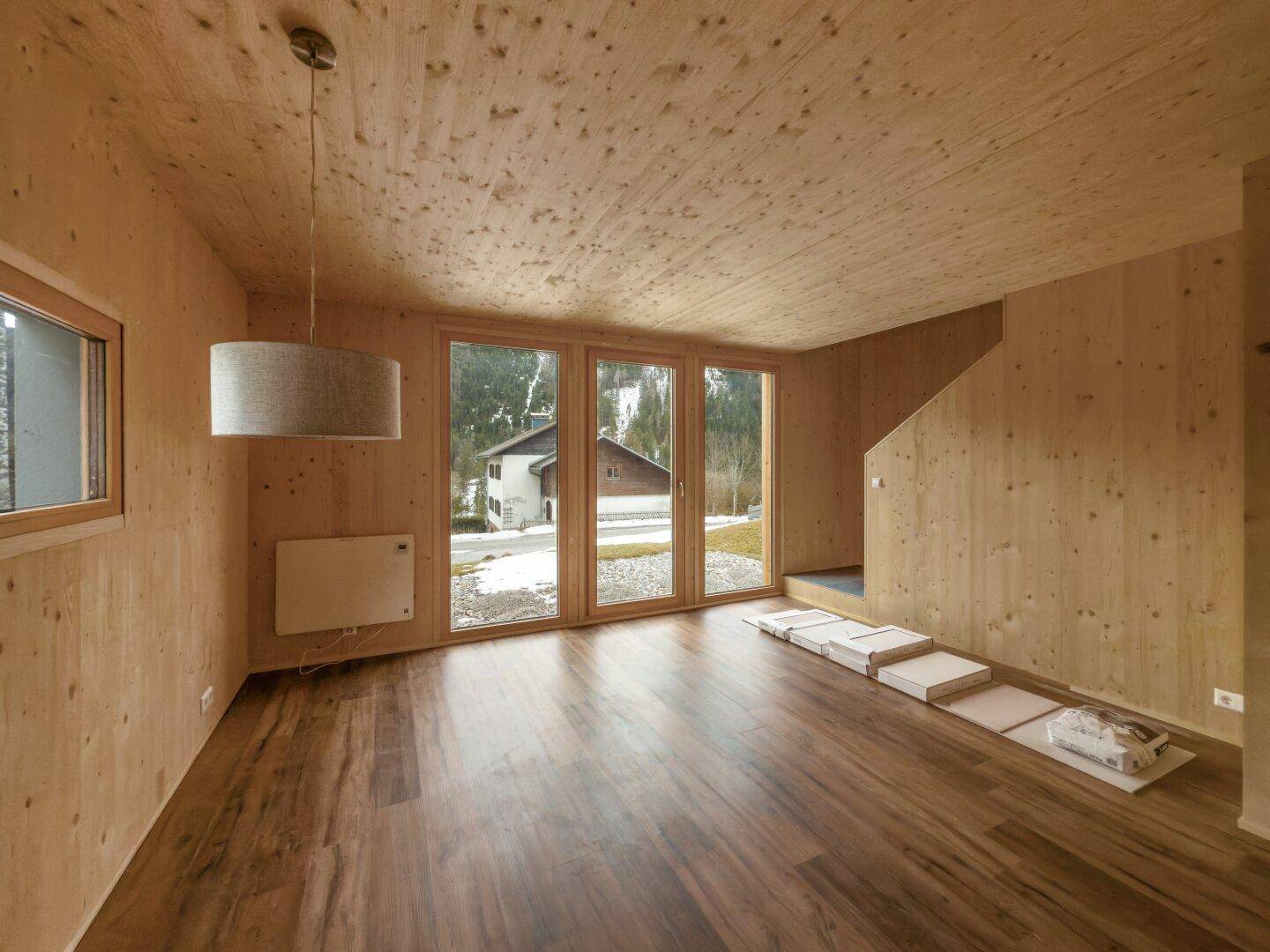 Heller Wohnraum mit Holzwänden, Holzdecke und großen Fenstern mit Blick ins Grüne.