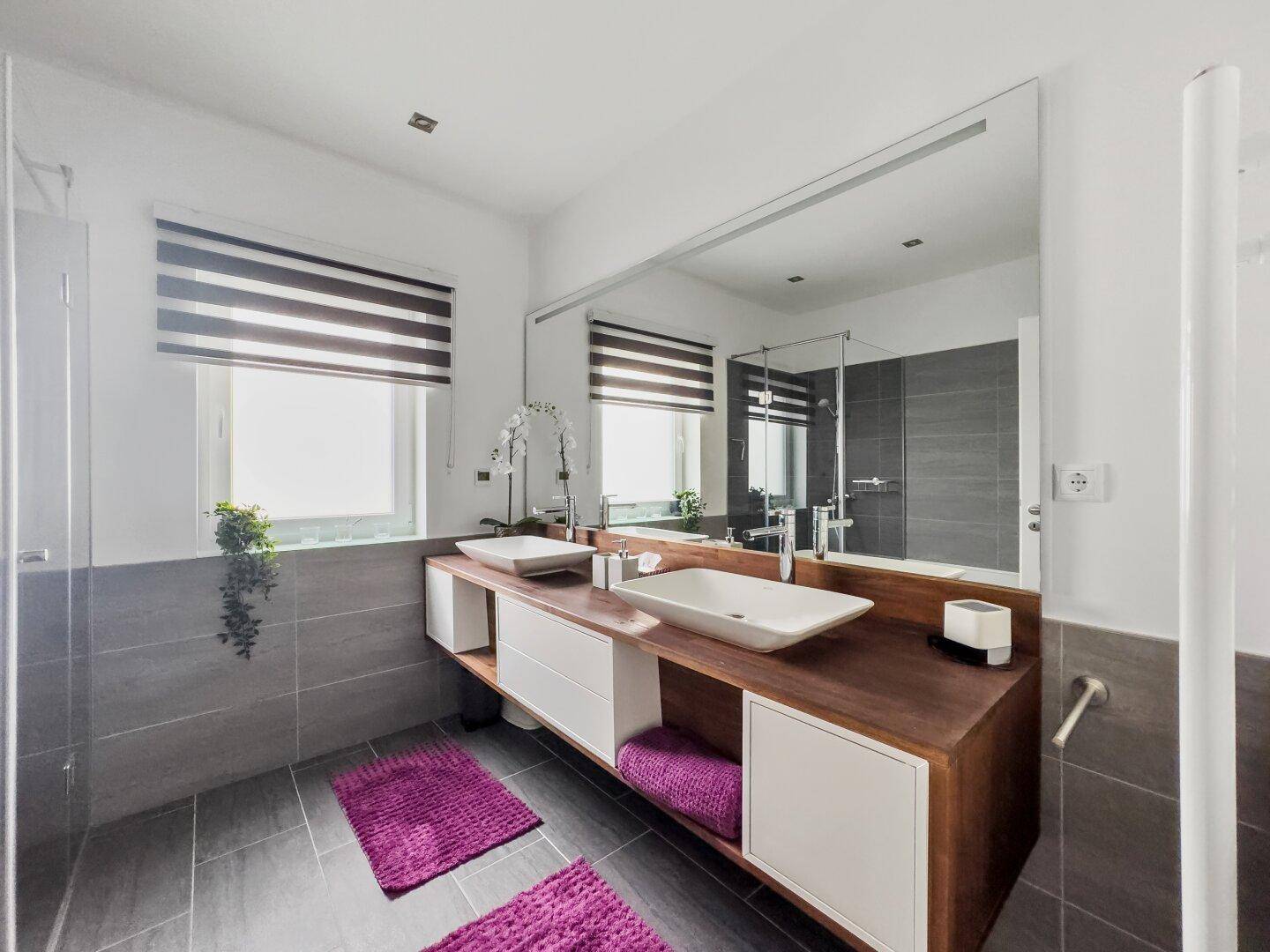 Modernes Badezimmer mit Doppelwaschbecken, großem Spiegel und grauen Fliesen.