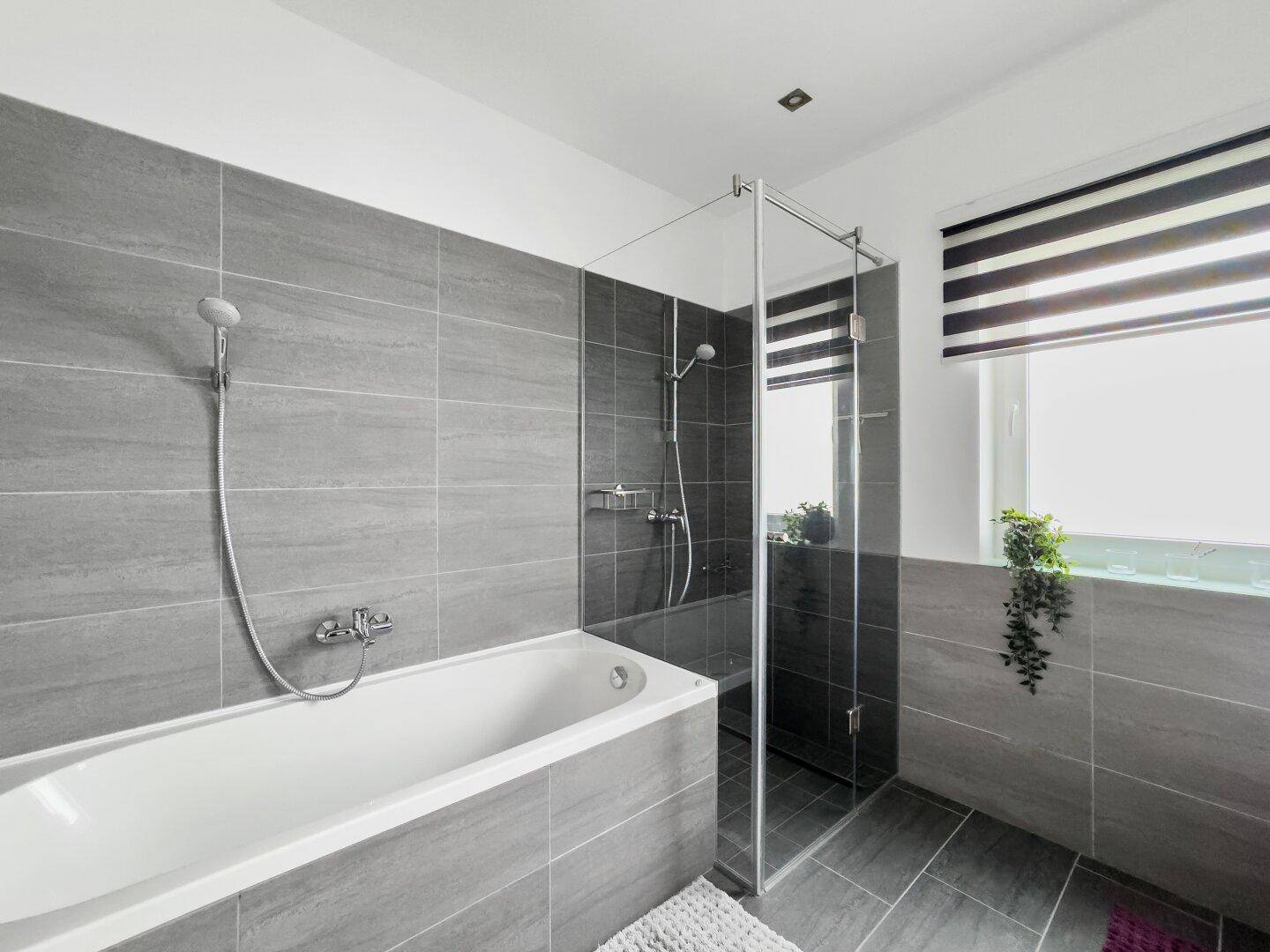 Helles Badezimmer mit Badewanne, separater Dusche und modernen grauen Fliesen.