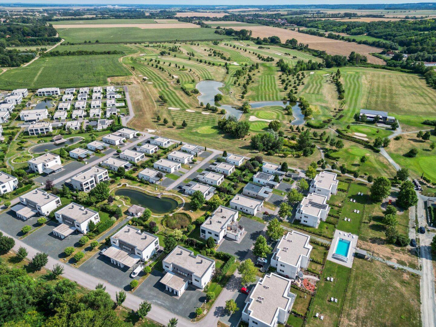Luftaufnahme der modernen Siedlung mit Gemeinschaftspool und Golfplatz im Hintergrund.
