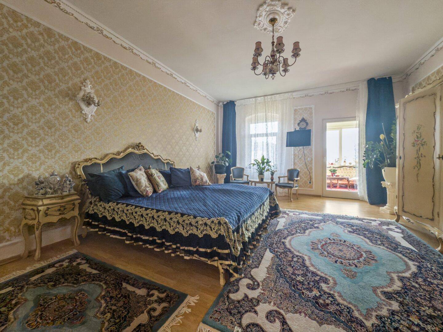 Luxuriöses Schlafzimmer mit großem Himmelbett, gemusterten Tapeten und Zugang zu einem Balkon.