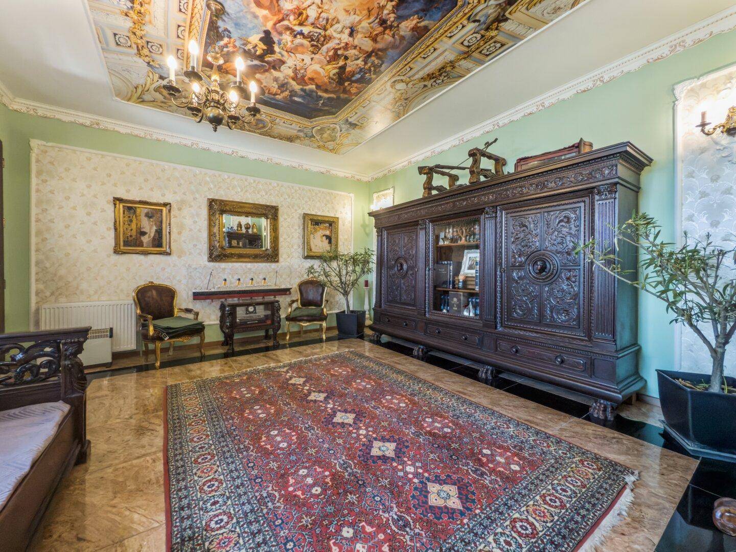 Repräsentatives Wohnzimmer mit großem, geschnitztem Holzschrank und bemalter Decke.