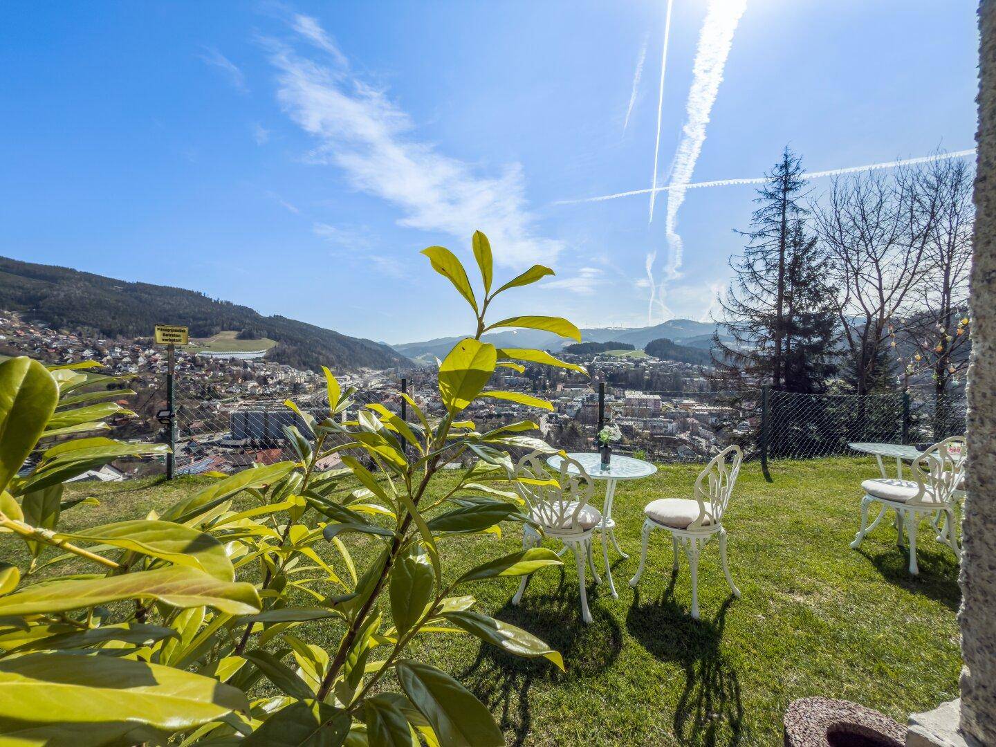 Sonniger Gartenbereich mit Sitzgelegenheiten und weitem Blick über die Stadt und die umliegende Landschaft.
