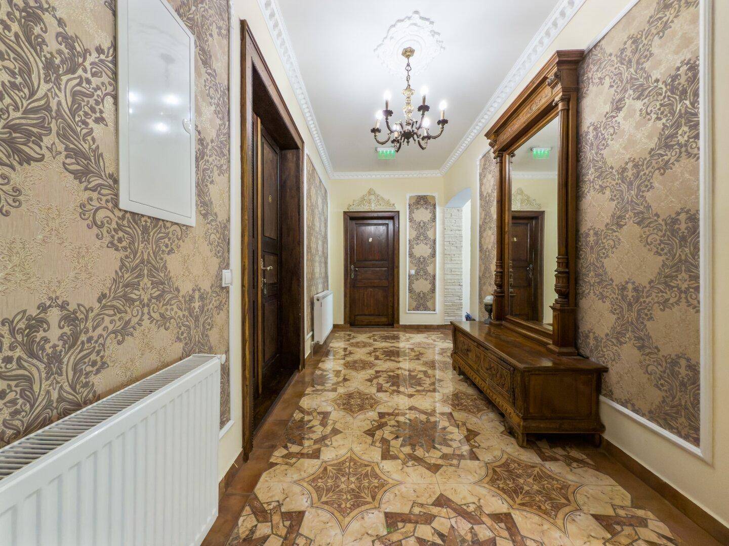 Heller Flur mit gemusterten Tapeten, elegantem Holzspiegel und glänzendem Fliesenboden.