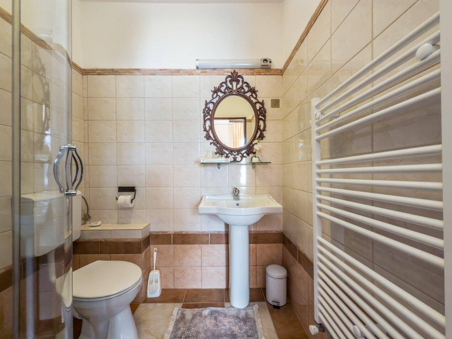 Helles Badezimmer mit beigefarbenen Fliesen, Standwaschbecken, Toilette und beheiztem Handtuchhalter.