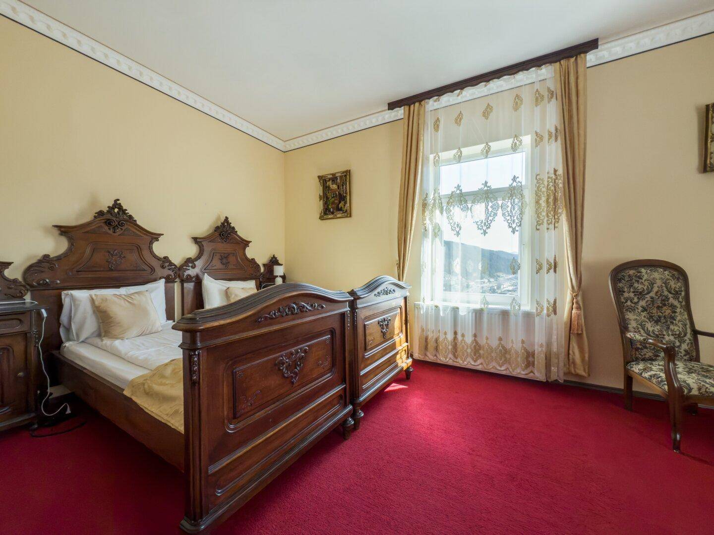 Gemütliches Schlafzimmer mit traditionellem Holzdoppelbett, rotem Teppichboden und Fenster mit Ausblick.