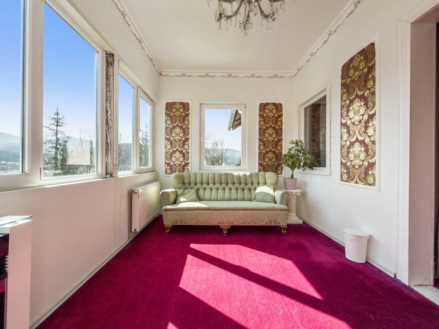 Geräumiges Wohnzimmer mit weitem Bergblick, großen Fenstern und einem grünen Sofa.