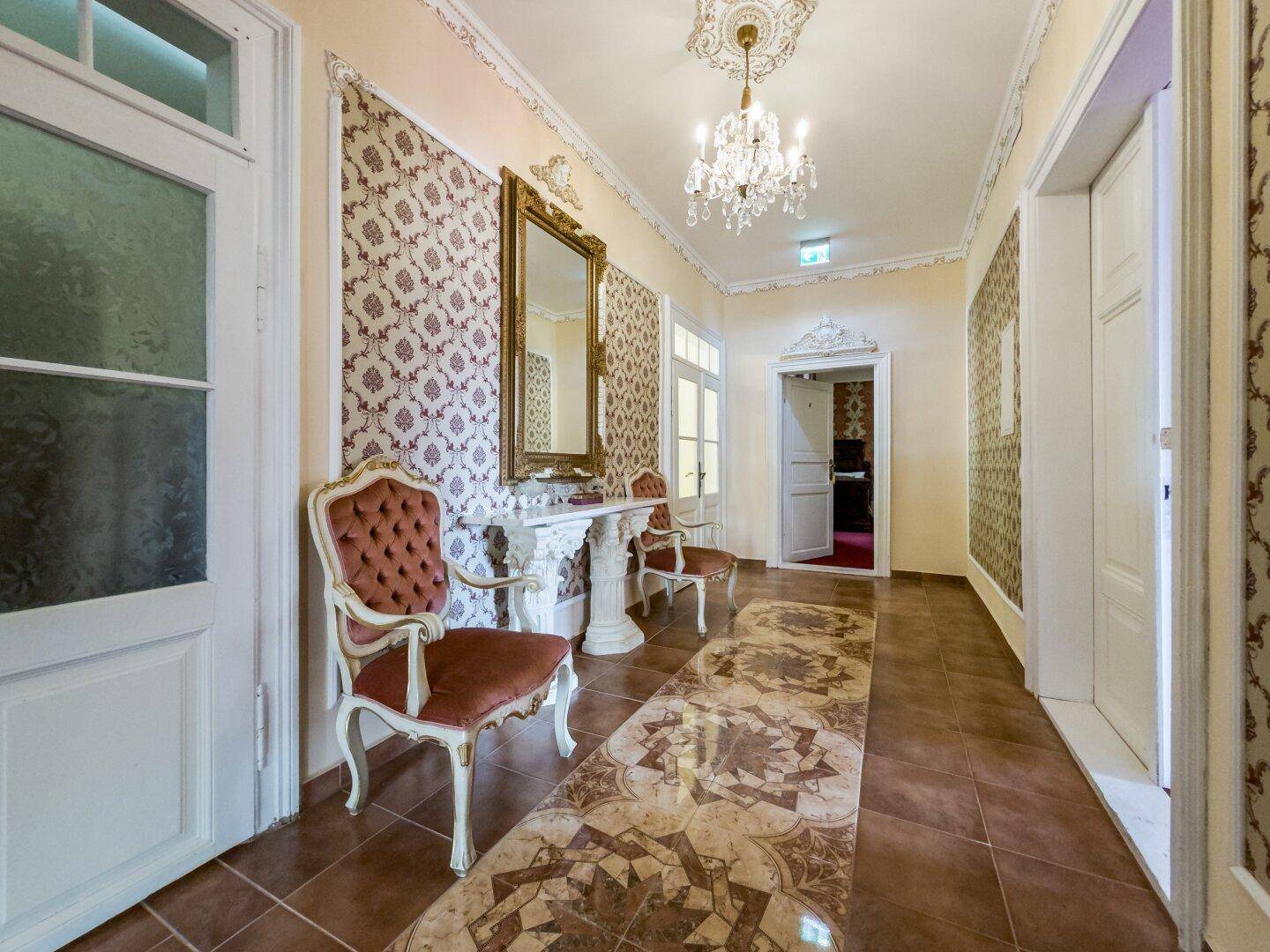 Eleganter Flur mit gemusterten Bodenfliesen, großem Spiegel und Kronleuchter.