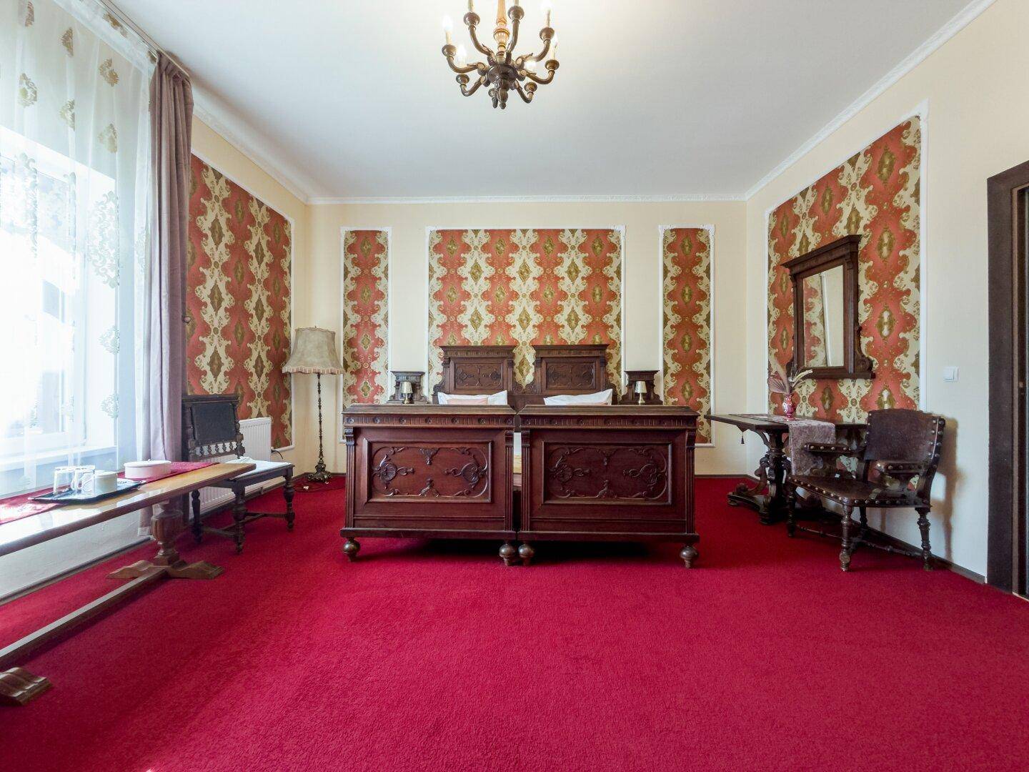 Schlafzimmer mit zwei Einzelbetten, rotem Teppichboden und traditioneller Tapete.