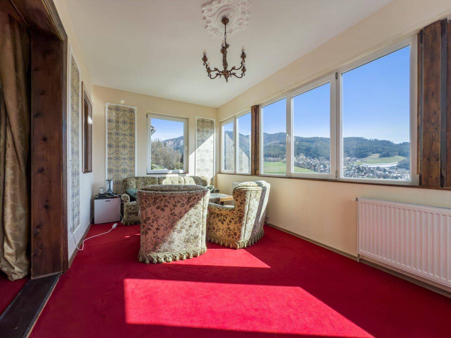 Helles Wohnzimmer mit Panoramablick auf die Berge, rosafarbenem Teppich und bequemen Sesseln.