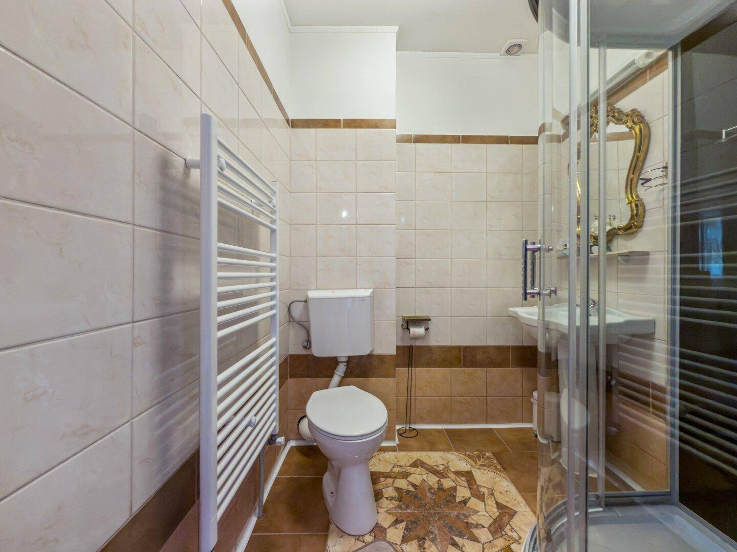 Badezimmer mit beigefarbenen Fliesen, Duschkabine, WC und beheiztem Handtuchhalter.