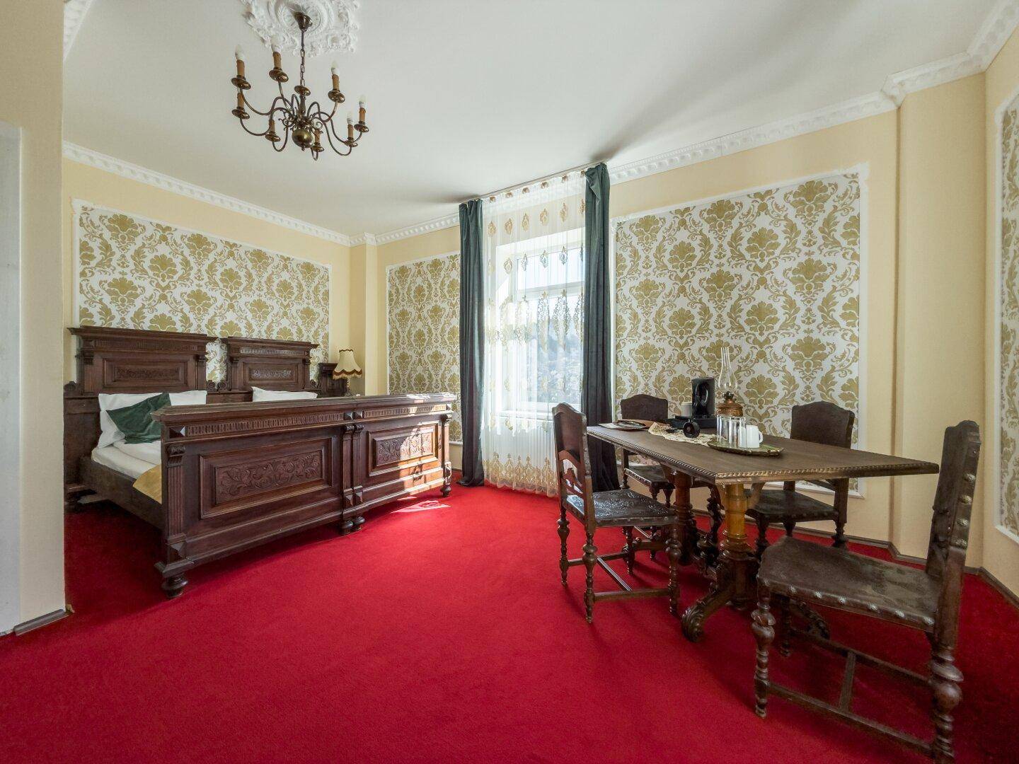 Schlafzimmer mit zwei Einzelbetten, rotem Teppichboden und einem Esstisch.