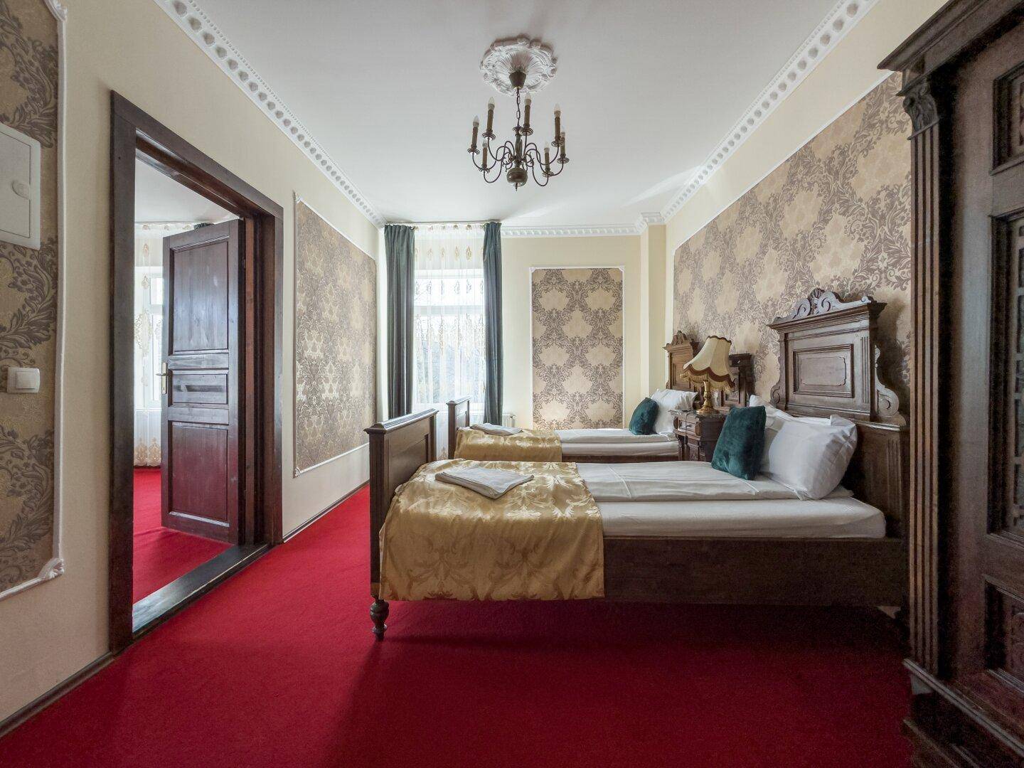 Schlafzimmer mit zwei Einzelbetten, rotem Teppichboden und Zugang zu einem weiteren Raum.