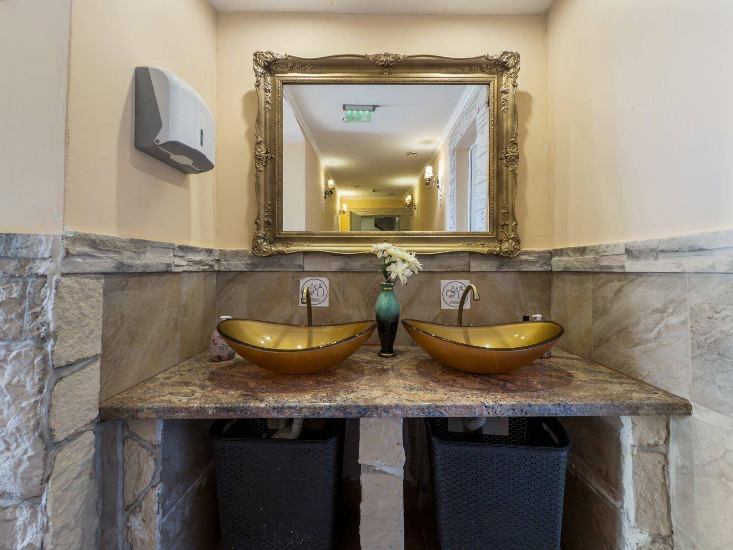 Elegantes Badezimmer mit zwei goldenen Aufsatzwaschbecken und einem verzierten Spiegel.