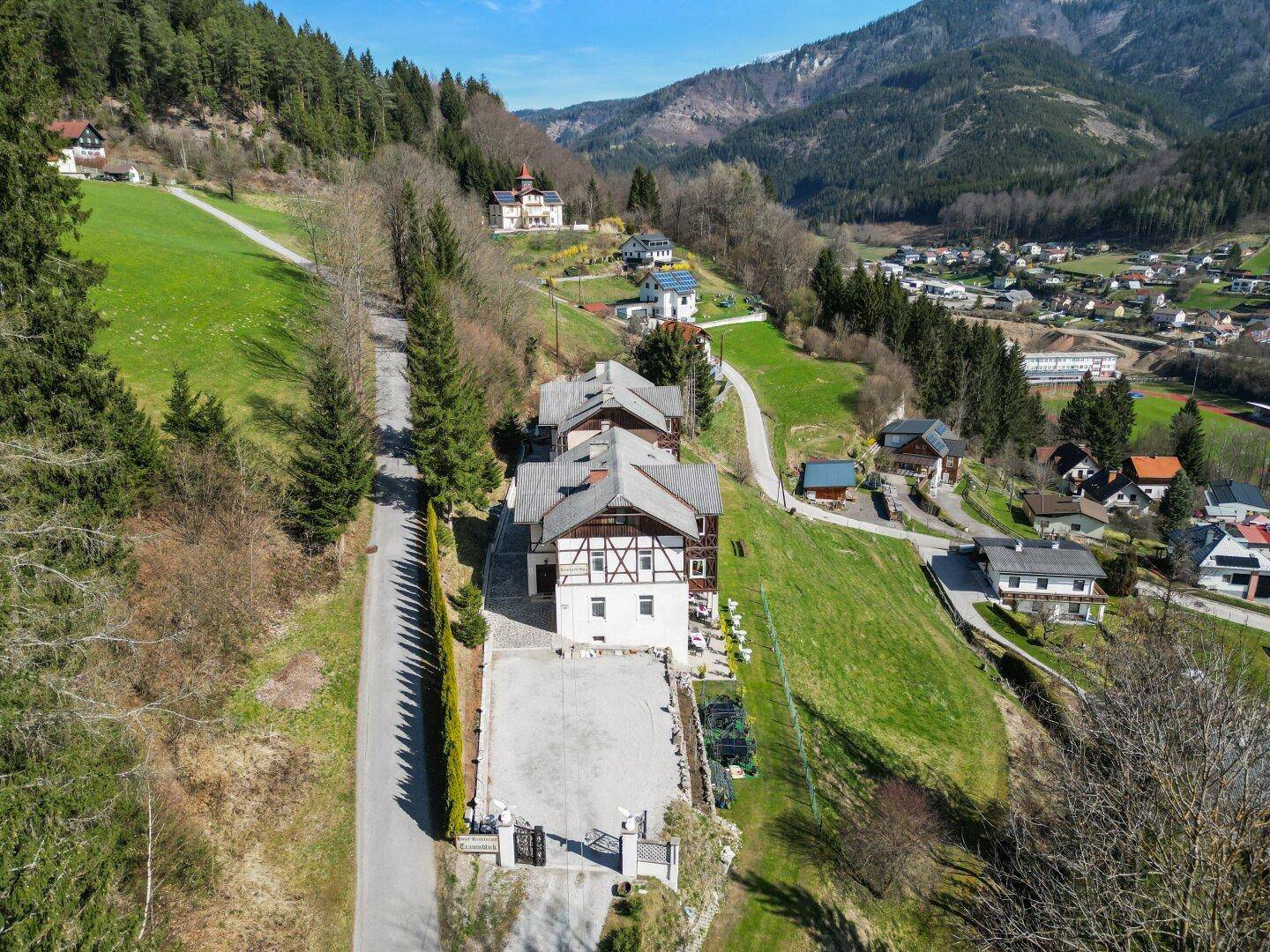 Luftaufnahme des Anwesens mit mehreren Gebäuden, umgeben von grünen Hügeln und einer Landstraße.
