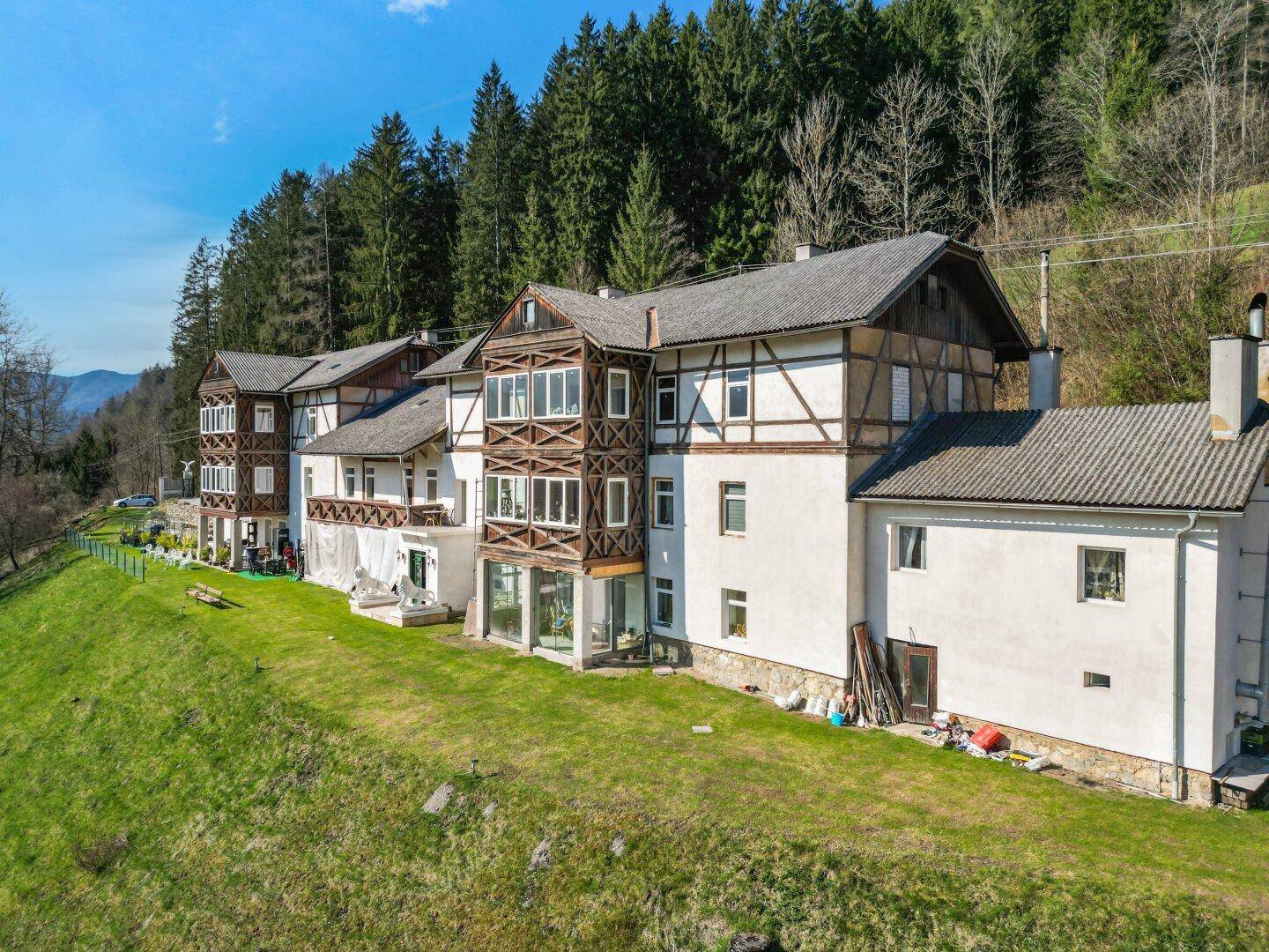 Ansicht der Gebäudeseite mit traditioneller Architektur und weitläufiger Grünfläche vor einem bewaldeten Hang.