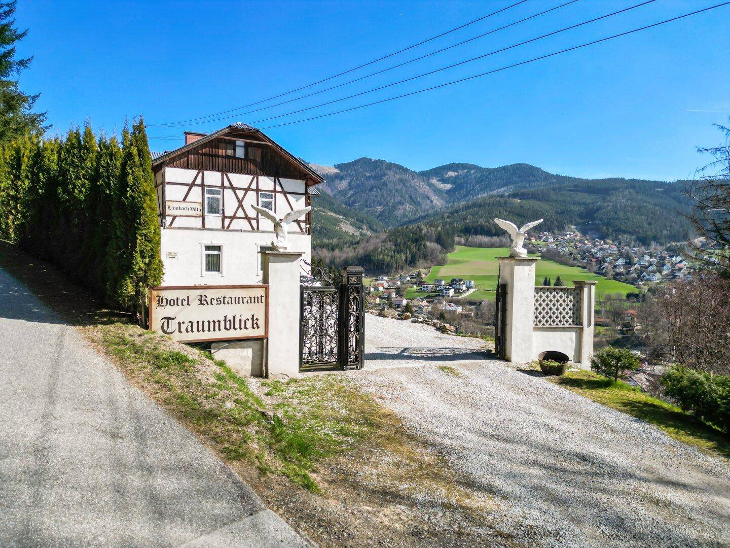 Einfahrtstor mit Skulpturen und weitem Blick über ein Tal mit einer kleinen Stadt und Bergen.
