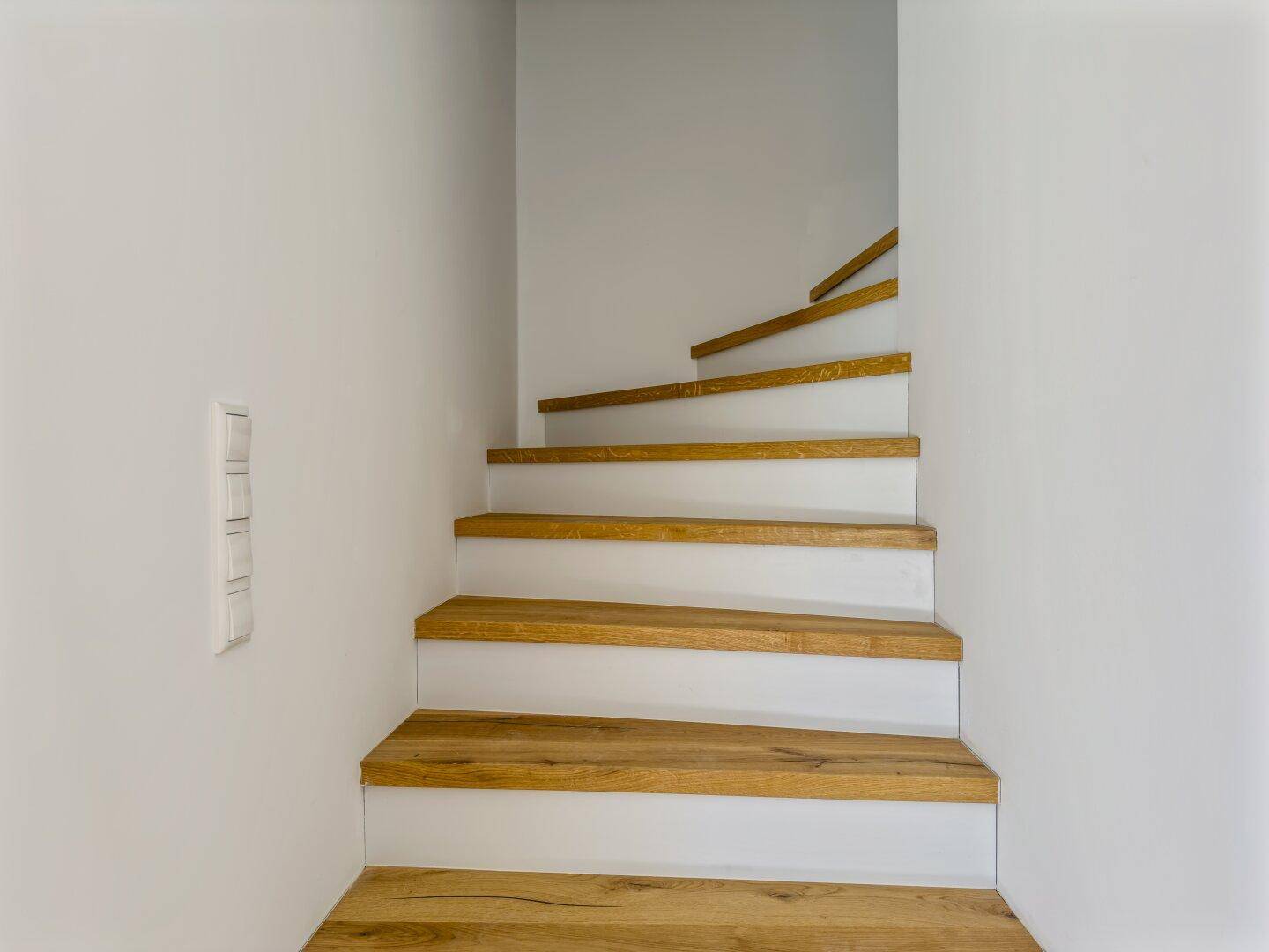 Moderne Holztreppe mit weißen Setzstufen, die elegant in das obere Stockwerk führt.