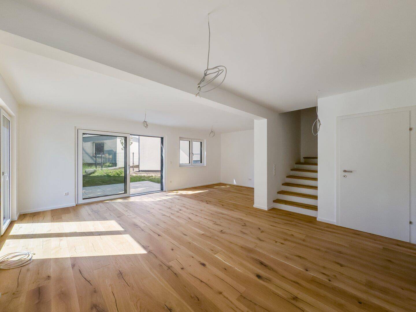Heller Wohnbereich mit Holzboden, Treppe und Zugang zu einer Außenterrasse, offen und einladend.