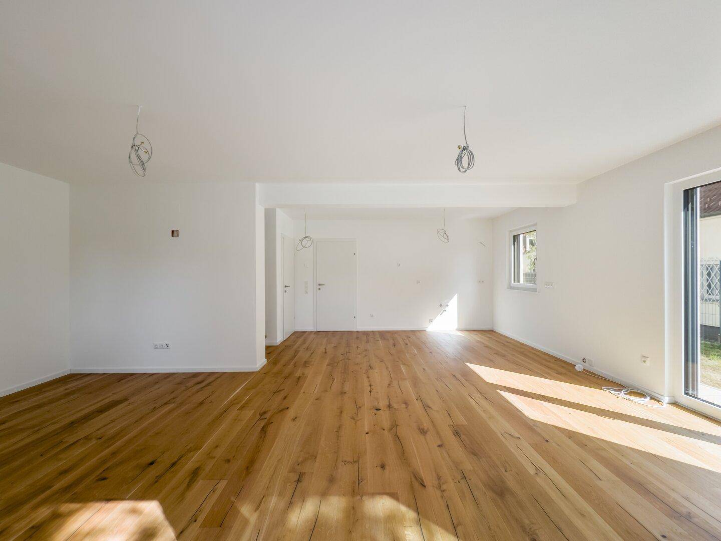 Geräumiger, unmöblierter Wohnbereich mit hellem Holzboden und viel Tageslicht, bereit zur Gestaltung.