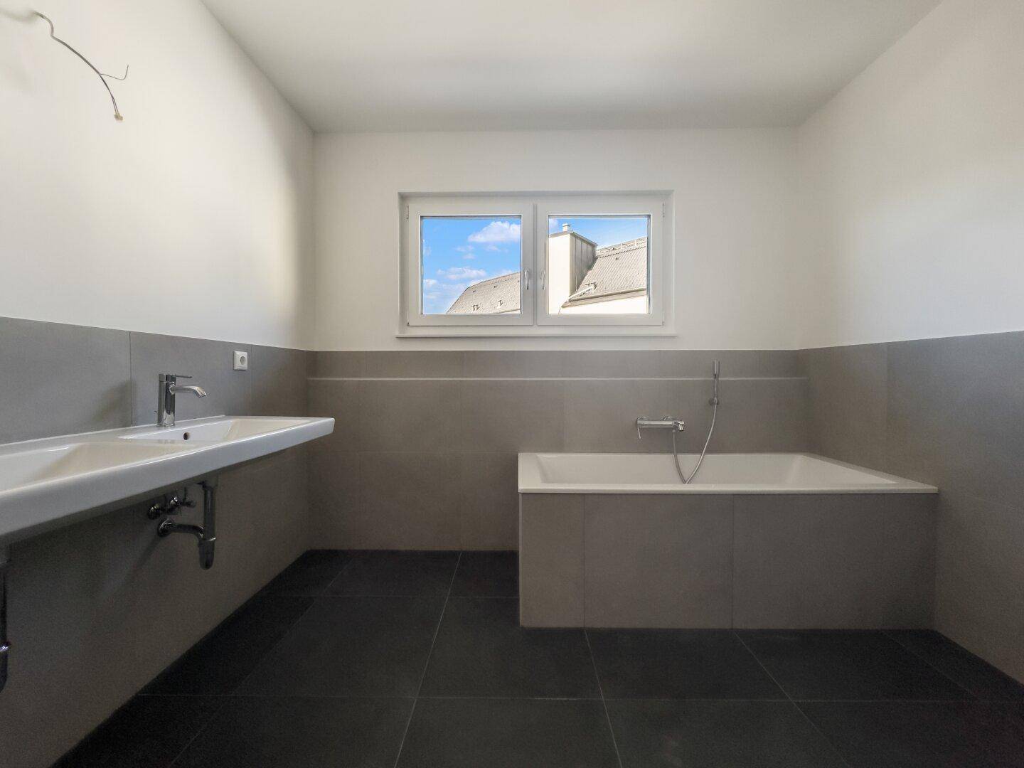 Helles Badezimmer mit Badewanne, Waschbecken und Fenster, das Tageslicht spendet und eine ruhige Atmosphäre schafft.