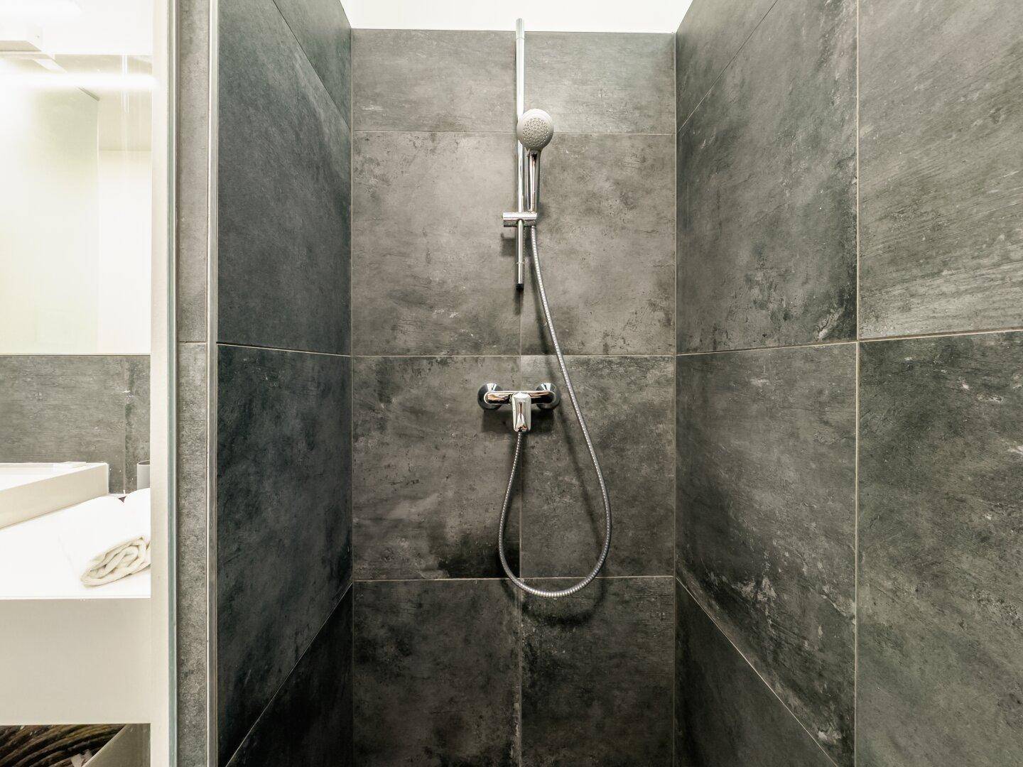 Geräumige Dusche mit dunklen Fliesen und moderner Armatur im Badezimmer.